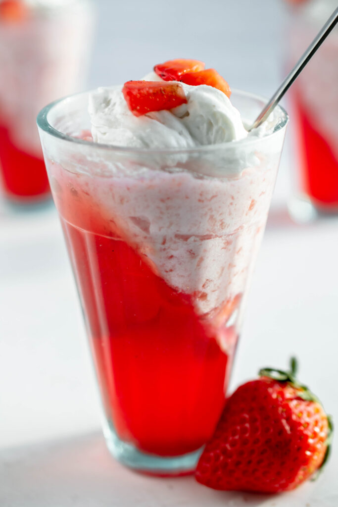 glass of strawberry jello parfait topped with whipped cream and diced strawberries