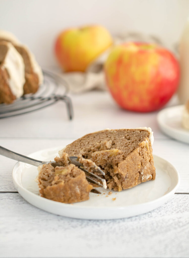 slice of apple bundt cake on a while plate with apples in the background