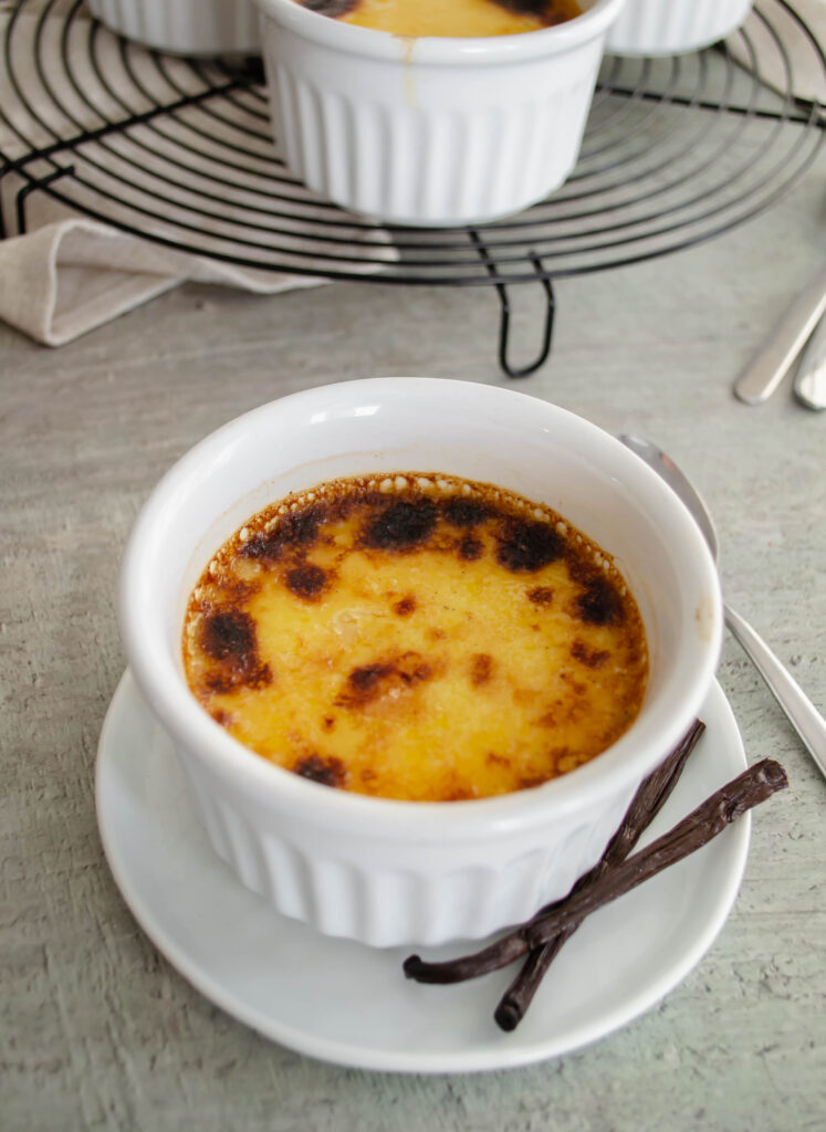 creme brulee in a white ramekin with vanilla beans on the side
