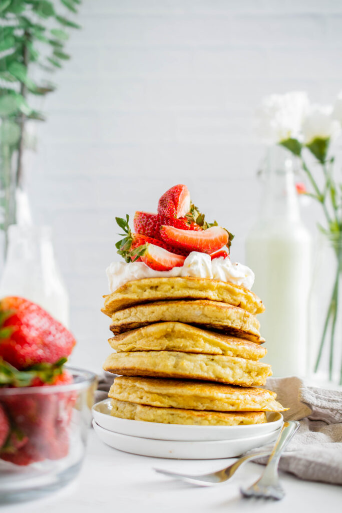 stack of almond flour pancakes topped with whipped cream and strawberries