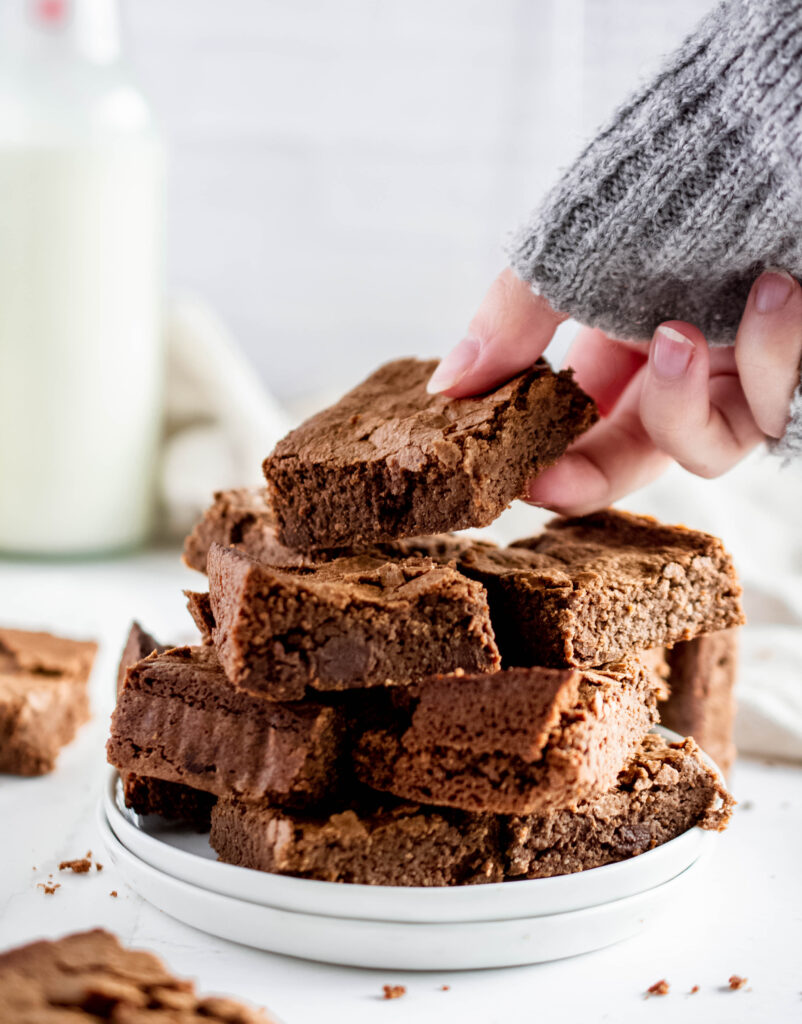 hand reaching for a stack of keto gluten free brownies on a white plate