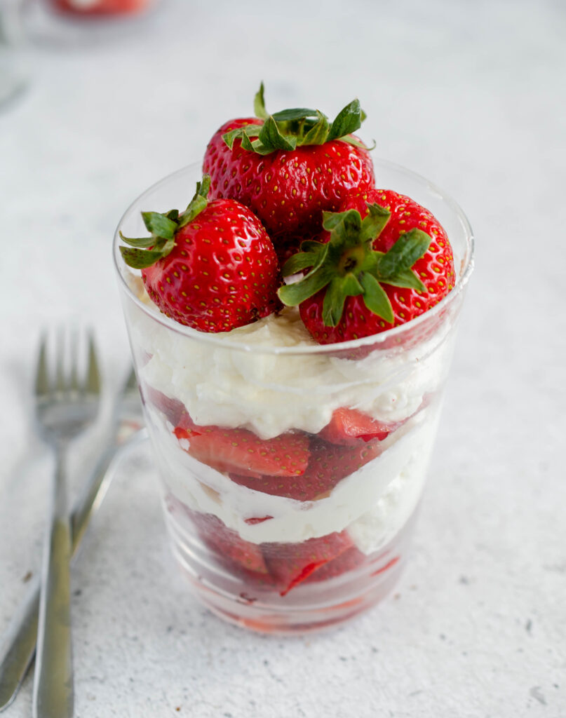 glass of layered diced strawberries and whipped cream