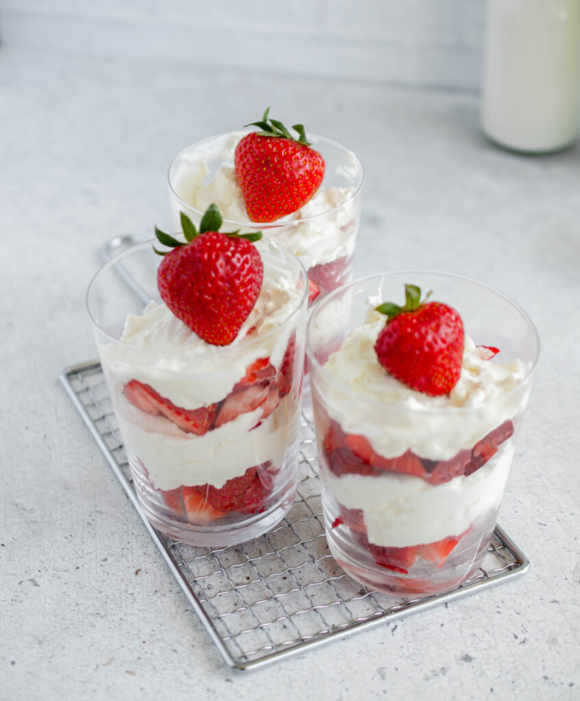 3 layered strawberry and cream desserts in glasses placed on top of a small cooling rack