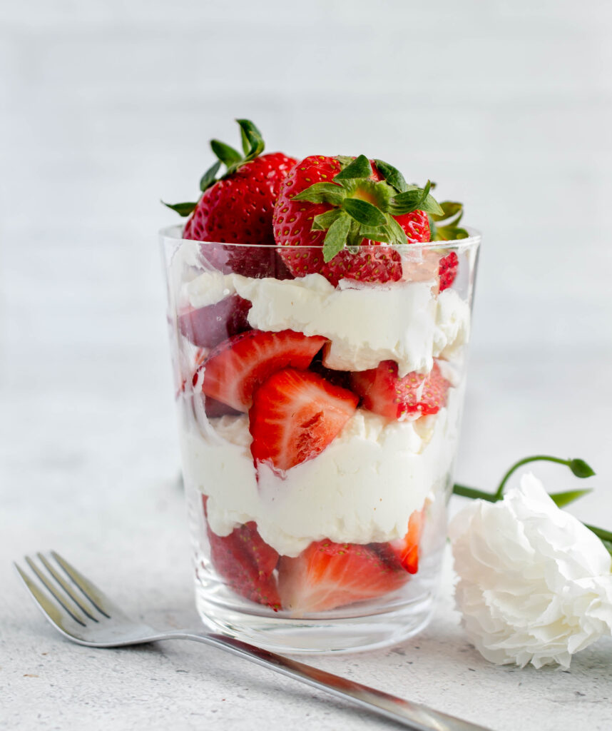 glass of layered diced strawberries and whipped cream