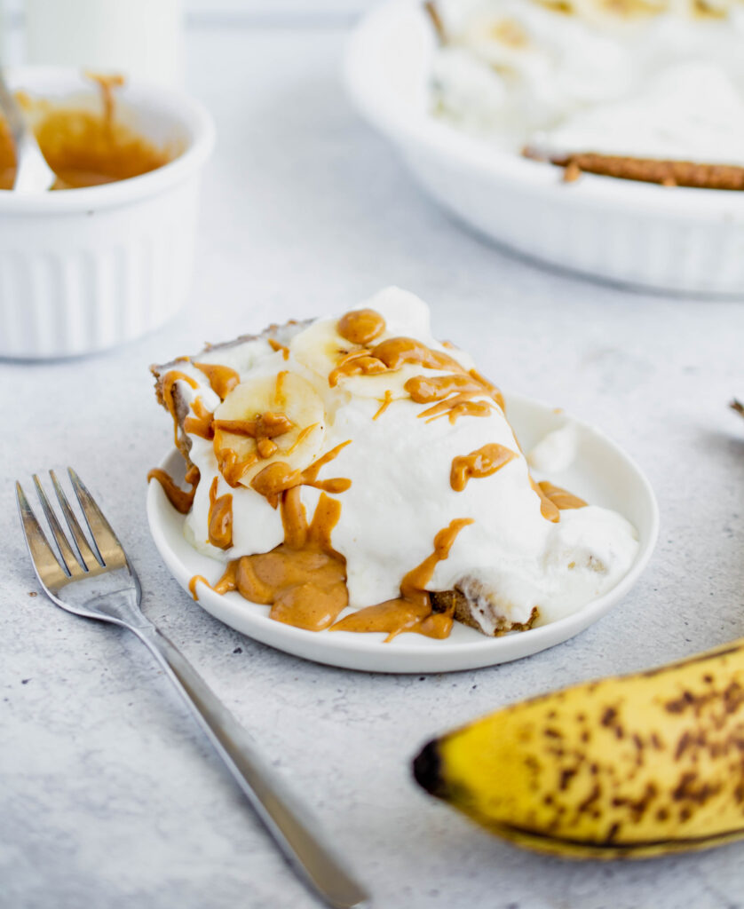 slice of banana cream pie topped with sliced bananas and drizzled with peanut butter