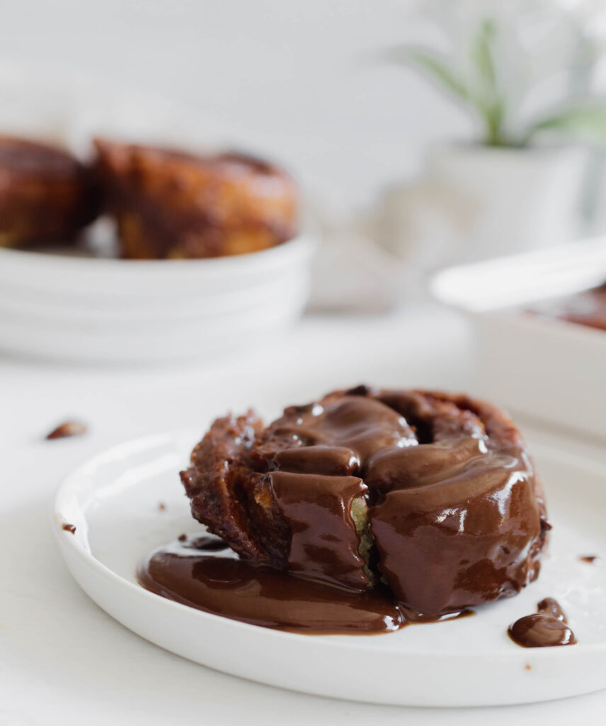 chocolate sticky bun on a white plate topped with melting chocolate
