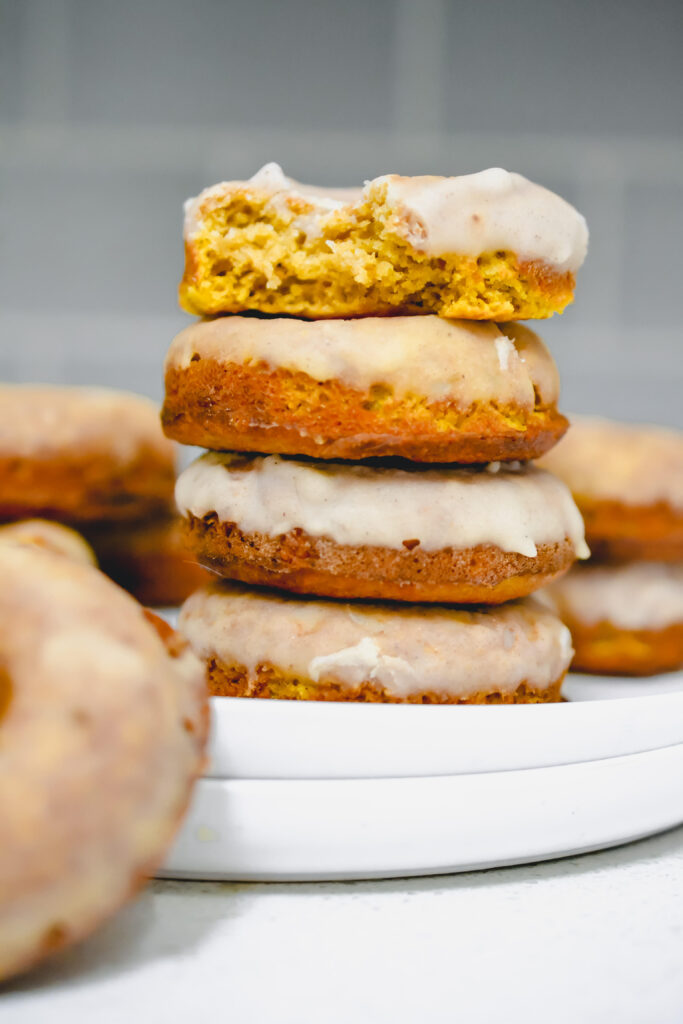 stack of pumpkin donuts, top donut has a bite taken out of it