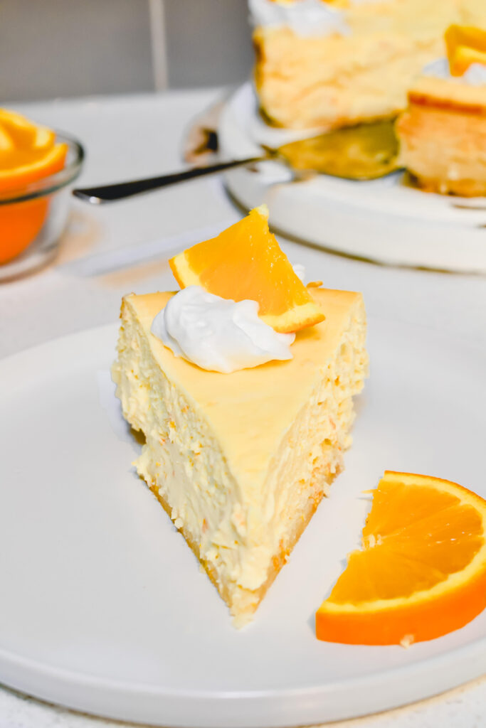Slice of orange cheesecake topped with whipped cream and a orange wedge
