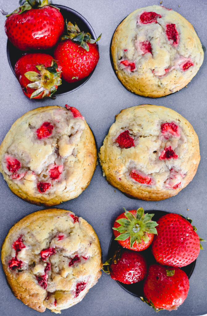 overhead photo of strawberry muffins in a muffin tin with strawberries in one muffin cup