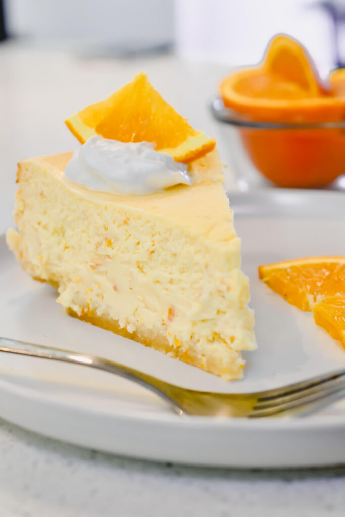 Slice of orange cheesecake topped with whipped cream and an orange wedge