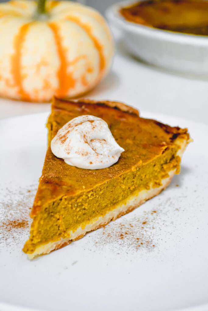 Slice of pumpkin pie topped with whipped cream and dusted with cinnamon