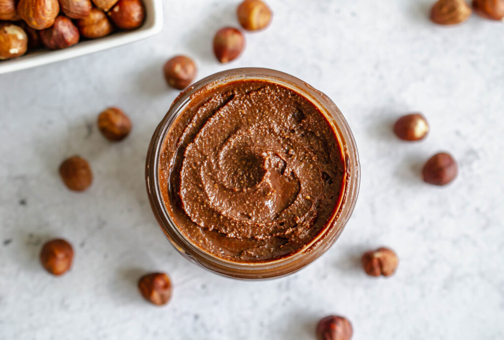 overhead photo of homemade nutella in a jar surrounded by hazlenuts
