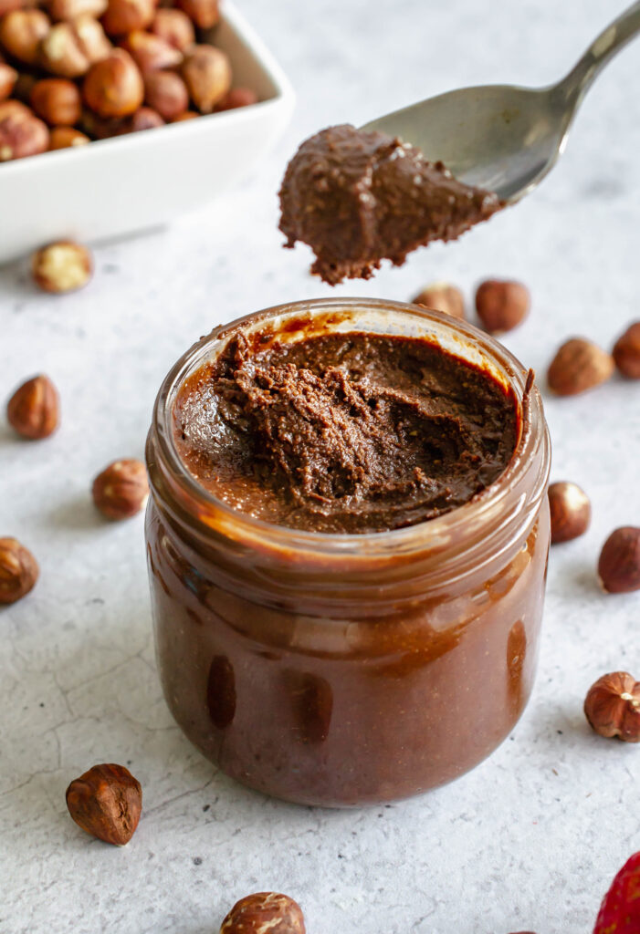 Small jar of homemade nutella with a spoon taking a scoop out of jar