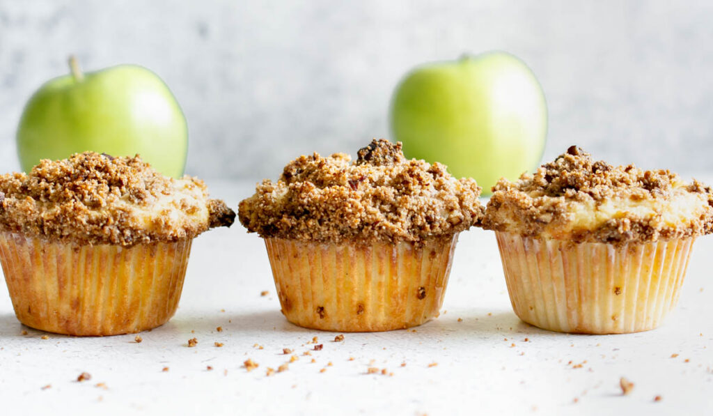 line of 3 gluten free apple crumble muffins with apples in the background