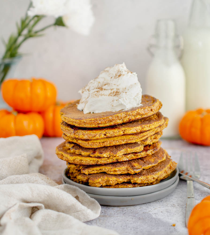 stack of Gluten Free Keto Pumpkin Pancakes topped with whipped cream and ground cinnamon