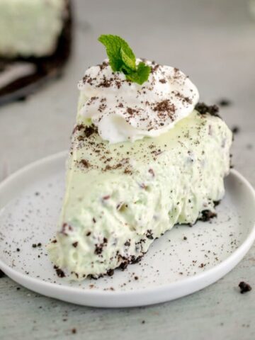 slice of Mint Chocolate Cheesecake topped with whipped cream and a mint leaf