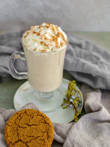 Keto Eggnog topped with whipped cream on a white plate with a gingerbread cookie