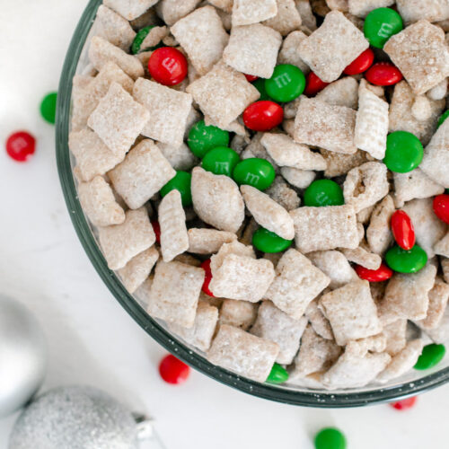 christmas puppy chow in a bowl surrounded by christmas ornaments