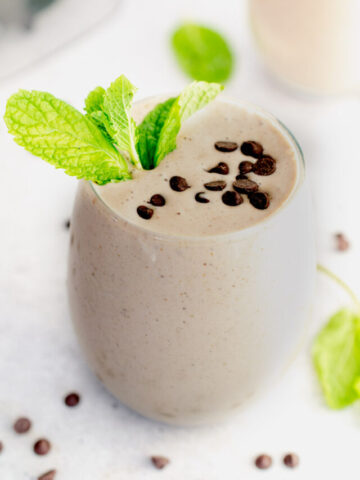 chocolate mint smoothie in a glass topped with mint leaves and chocolate chips