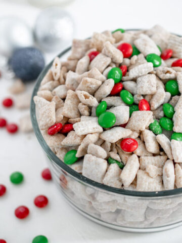 christmas puppy chow in a bowl surrounded by christmas ornaments