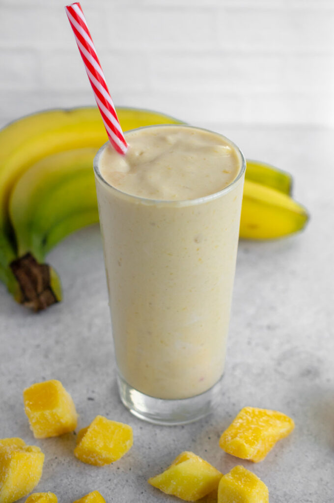 glass of banana peach smoothie with a straw