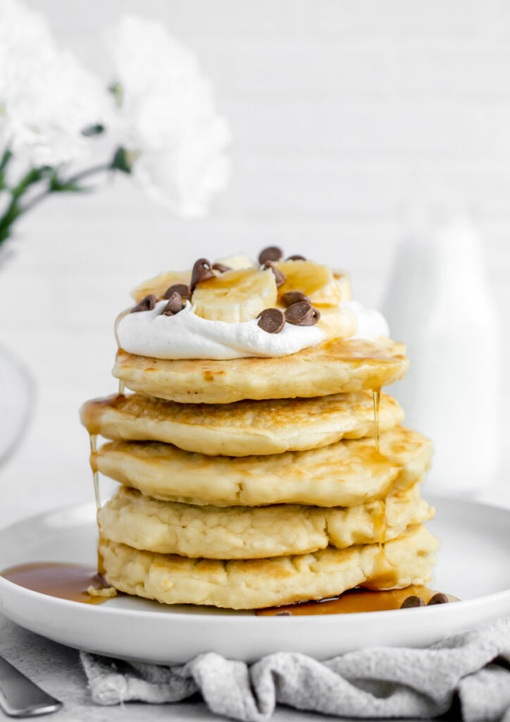 stack of dairy free pancakes topped with bananas and dairy free whipped cream