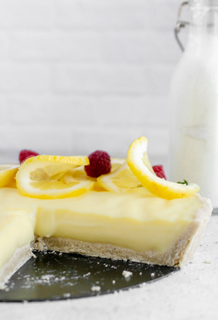 vegan lemon tart topped with sliced lemon and raspberries