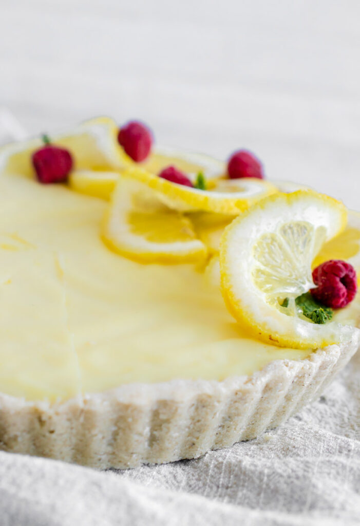 vegan lemon tart topped with sliced lemon and raspberries